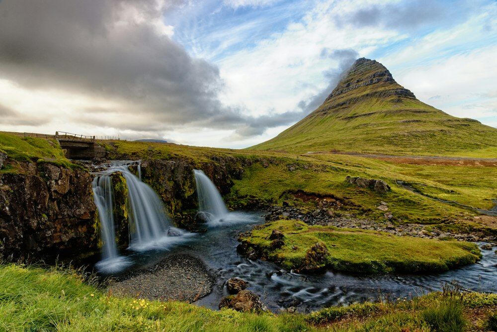 green grass field near waterfalls under cloudy sky during daytime